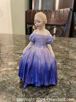 Front view showing the detailed facial features, purple puff-sleeve dress, and seated pose of the Royal Doulton Marie figurine