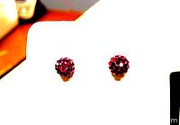 Close-up image of a pair of round red stud earrings with shiny Swarovski crystals clustered on gold plated posts, shown on white display card.