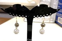 Pair of two-tone Swarovski crystal ball dangle earrings on a black display stand.
