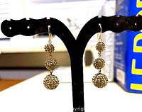 Pair of gold plated Swarovski crystal earrings with triple ball design on display stand.