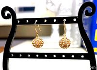 Pair of Swarovski crystal earrings hanging on a decorative black display stand, showing gold plated hooks and spherical brown crystal beads.