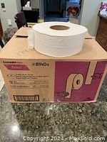 Image showing a large industrial toilet paper roll placed on top of a box labeled Cascades Pro Select B140B, with box showing product details and diagrams.