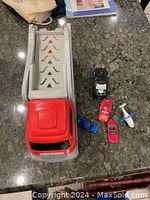 Toy car transport truck alongside five toy vehicles, including cars and a helicopter, placed on a dark granite countertop.