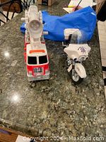 Red and white toy fire truck and white toy police motorcycle placed side by side on a granite countertop.