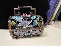 Closed trinket box showing colorful floral and dragonfly motifs with crystals around edges and handle on top.