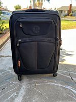 Front view of black carry-on suitcase showing front pocket with zipper, orange tag, and stitching detail.