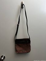 Full view of the crossbody purse hanging on a hook, showing the adjustable black strap, patterned fabric body, and front zipper pocket with black trim.