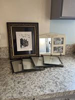 Six picture frames on a countertop including a large ornate frame, medium triple window frame, and four smaller black frames.