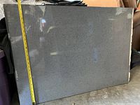 Granite slab measuring approximately 36 inches by 25 inches, grey with small dark speckles. Polished surface reflecting light.