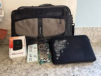 Photo showing a black and gray laptop bag, a black tablet sleeve with white design, two transparent iPhone 13 cases with panda designs, and a boxed mobile hotspot device on a countertop.