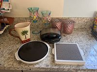 Photo showing ceramic pitcher, two decorative glass vases, sandwich grill, and two defrosting plates on countertop.