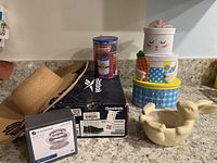 Photo showing the complete lot set of items on a granite countertop including Reebok shoes, straw hat, sink strainer box, spa filter box, ceramic bunny planter, and stacked bunny gift boxes.