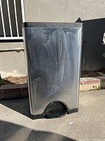 Front view of a rectangular stainless steel trash can showing rust spots and a black pedal.