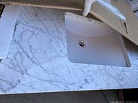 White and gray marble-patterned vanity top with integrated sink basin, displayed packed partially in cardboard box.