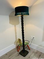 Full view of the lamp showing the tall spiral wooden carved post, square base, and the green fabric drum lampshade with fringe.