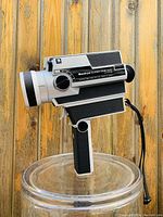 Front-side angle showing Sankyo Super 8 CME 440 camera body with manual focus and zoom rings, trigger, textured grips, and wrist strap.