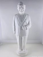 Front full-length view of white Colonel Sanders figurine with cane on a plain background.