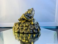 Side view of heavy metal Chinese Feng Shui money toad statue on coin base showing intricate coin detail and three-legged toad with red accents.