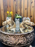 Photo showing both horse head shaped desk items on a decorative metal stand with wooden backdrop and plants in the background.