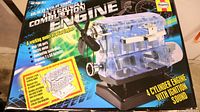 Front of the box showing the kit name, features, images of the transparent 4-cylinder engine model with fan and stand, and key product details.