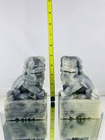 Front and side view of two marble Fu Dog statues showing detailed faces, manes, and sitting poses, positioned near a measuring tape showing approximately 7 inches in height.