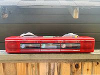 Front view of closed triple cassette compartments on red stereo unit with branding and control buttons on top.