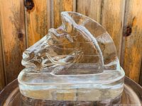 Side profile view of solid clear glass horse head sculpture showing detailed facial and mane features on a thick rounded base.