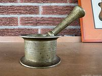 Side view of antique brass mortar with pestle resting on the mortar rim, showing the cylindrical shape and textured surface.