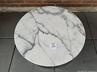 Top-down view of round white marble table top showing grey veining and auction sticker.