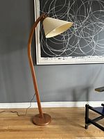 Full view of the teak arc floor lamp standing against a gray wall and wood floor.