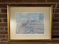 Framed limited edition print showing the entire artwork in a gold frame hung on a brick wall.