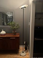 Full view of the floor lamp showing black metal pole, frosted white glass shade and white glass base