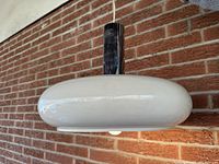 Side view showing pendant light hanging against a brick wall with light bulb illuminated under the white enameled donut-shaped metal shade.