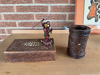 Front view showing the carved wooden box, painted warrior figurine, and carved wooden cup