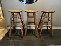 Front view of three oak swivel bar stools, 30 inches tall, showing round seats and turned legs
