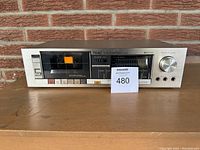 Front view of the Teac V-33 stereo cassette deck with tape inside compartment, showing the buttons, dial, and display.