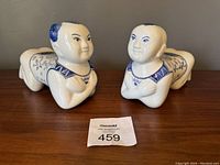 Full view of both vintage blue and white porcelain Buddha baby figurines lying on a surface, showing their size and design.