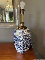 Full view of hexagonal blue and white porcelain table lamp base with brass fixture and light bulb socket on wooden surface.