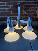 Front perspective view of the lamp showing four illuminated milk glass shades and chrome arms.