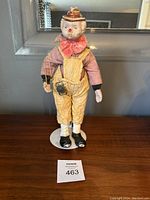 Front view of vintage clown doll standing on a white circular stand against a dark background.