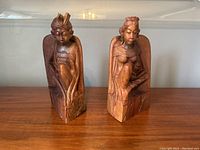 Pair of vintage hand carved teakwood book ends side by side on a wooden surface in front of a neutral wall.