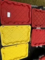 Five plastic storage tote lids in red and yellow stacked outdoors