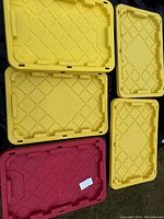 Photo of five yellow and red 27-gallon storage tote lids, empty and showing size reference for the boxes.