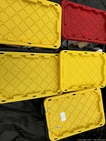 Five plastic storage tote lids in yellow and red colors stacked showing lot container size and quantity.