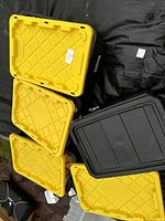 Five plastic storage totes with yellow and black lids, tops open and closed, labeled '16'