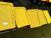 Five yellow 27 gallon tote lids arranged on grass, showing the size and number of containers in the lot.