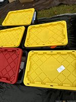 Five large storage totes with yellow and red lids arranged outdoors, showing lot number 5 on one lid.