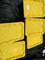 Five yellow plastic lids for large storage totes, stacked and arranged on black ground cover.