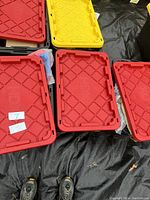 Photo showing five 27 gallon plastic storage totes with red and yellow lids, arranged on the ground