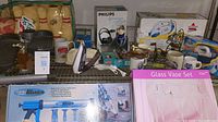 Wide angle view showing full lot including glass vase set, mugs, Bissell steam mop box, Philips headphones box, decorative items, and appliances.
